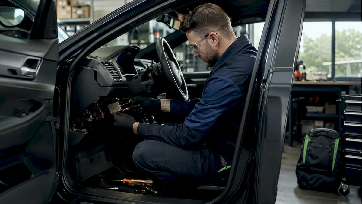 Technician installing car tracker under dashboard