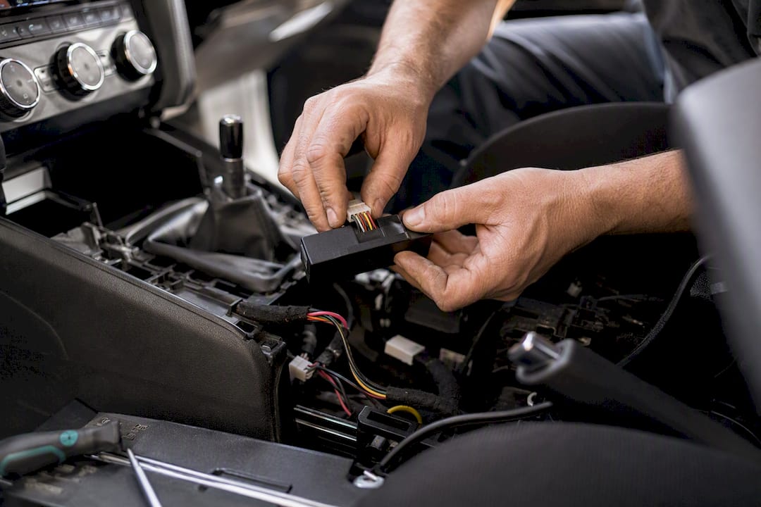 Hands installing vehicle tracker near dashboard
