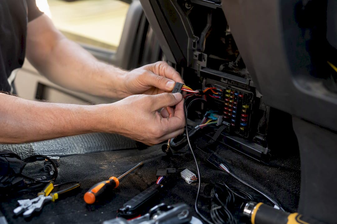 Hands wiring a vehicle fuse box for tracker installation
